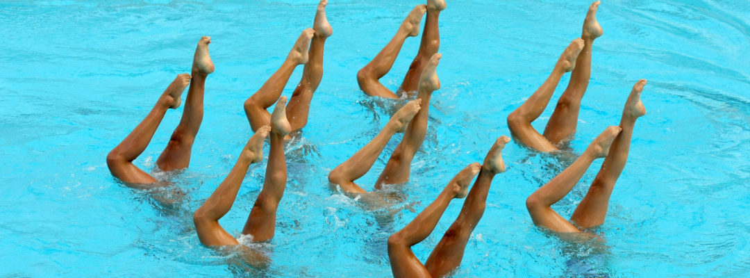 Synchronized Swimmers legs point up out of the water in action